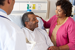 older gentleman laying in hospital bed looking at woman and doctor