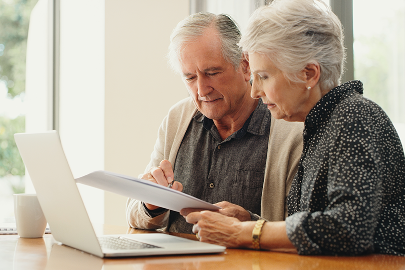 older couple looking at paperwork in front of a computer