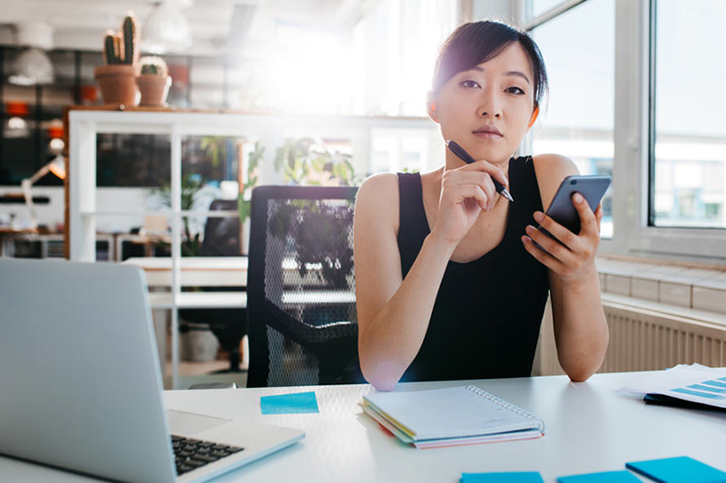 woman with a pen and notebook holding her phone