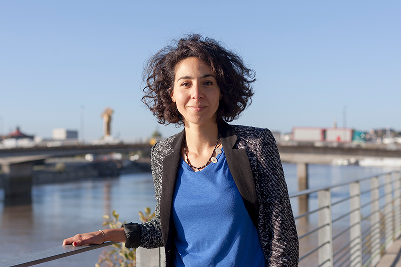 woman standing outside leaning against a railing looking at camera