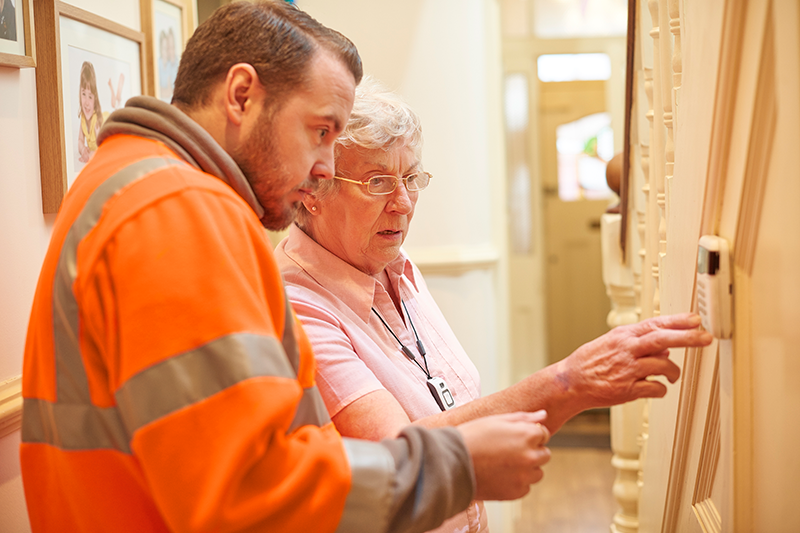 maintenance man and older woman looking at thermostate on wall of building