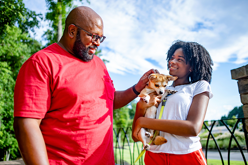 man petting a small dog that is being held by a young girl 