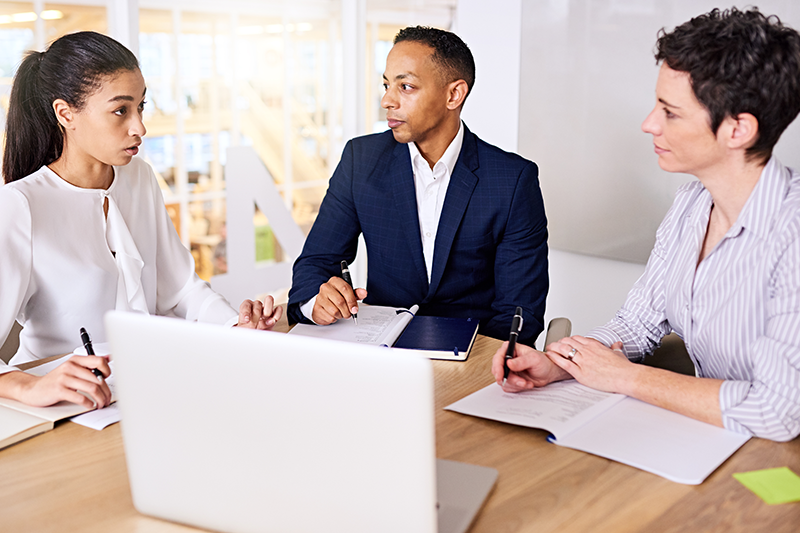 three adults at table talking with computer